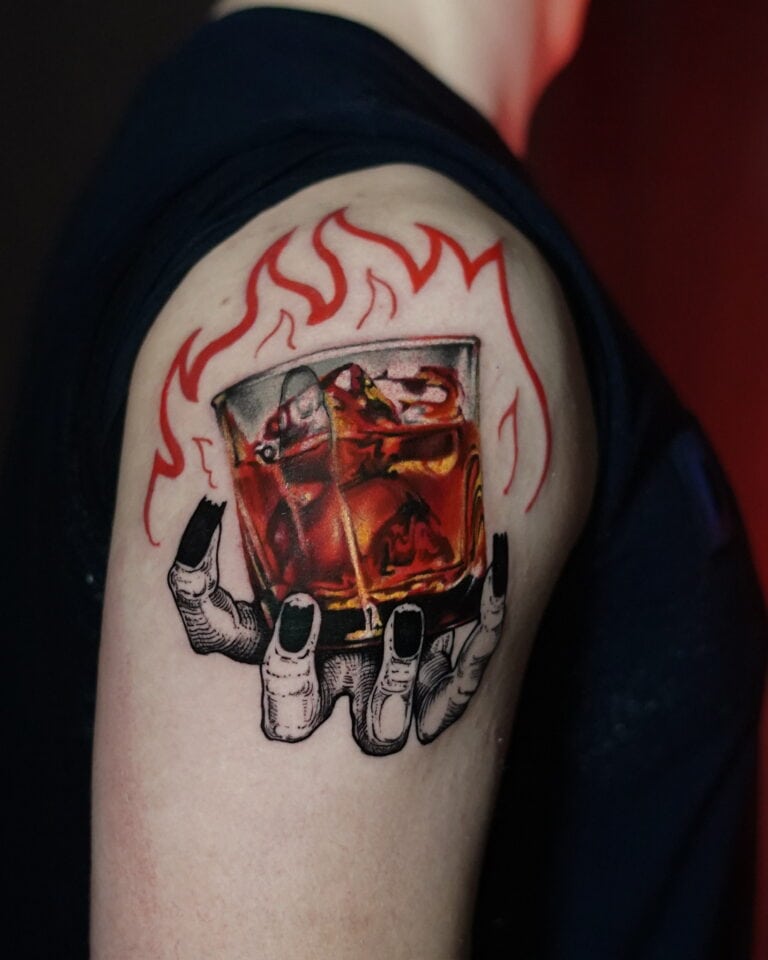 Tatuaż na górnej części ramienia przedstawia dłoń z czarnymi paznokciami trzymającą szklankę whisky z kostkami lodu. Czerwone płomienie otaczają szklankę, tworząc ognisty efekt. Aby uzyskać skomplikowane wzory, takie jak DSC00018, odwiedź Najlepsze Studio Tatuażu Poznań w Seven Sins Tattoo, aby mieć pewność, że Twoja sztuka na ciele wyróżni się wyjątkowym detalem i kunsztem wykonania.