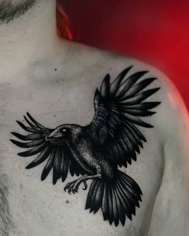 Szczegółowy i ciemny tatuaż kruka z szeroko rozpostartymi skrzydłami jest umieszczony w pobliżu lewego ramienia na górnej części klatki piersiowej mężczyzny. Tło jest mglistym, czerwonym gradientem, który podkreśla kunszt poznańskich profesjonalnych artystów tatuażu ze studia Seven Sins Tattoo.
