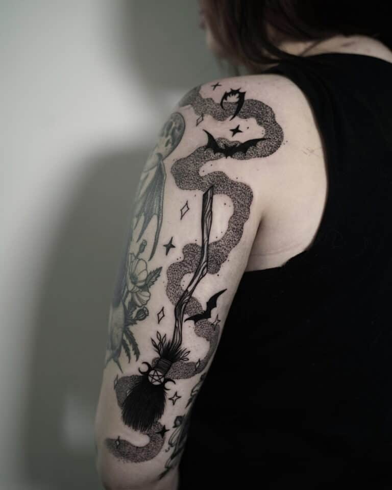 Długowłosy osobnik ma na sobie czarny top bez rękawów, z misternym czarnym tatuażem na górnej części ramienia. Tatuaż, wykonany w najlepszym poznańskim studiu Seven Sins Tattoo, zawiera różne obrazy, w tym nietoperze, kapelusz czarownicy i wirujące wzory w stylu DSC00373.