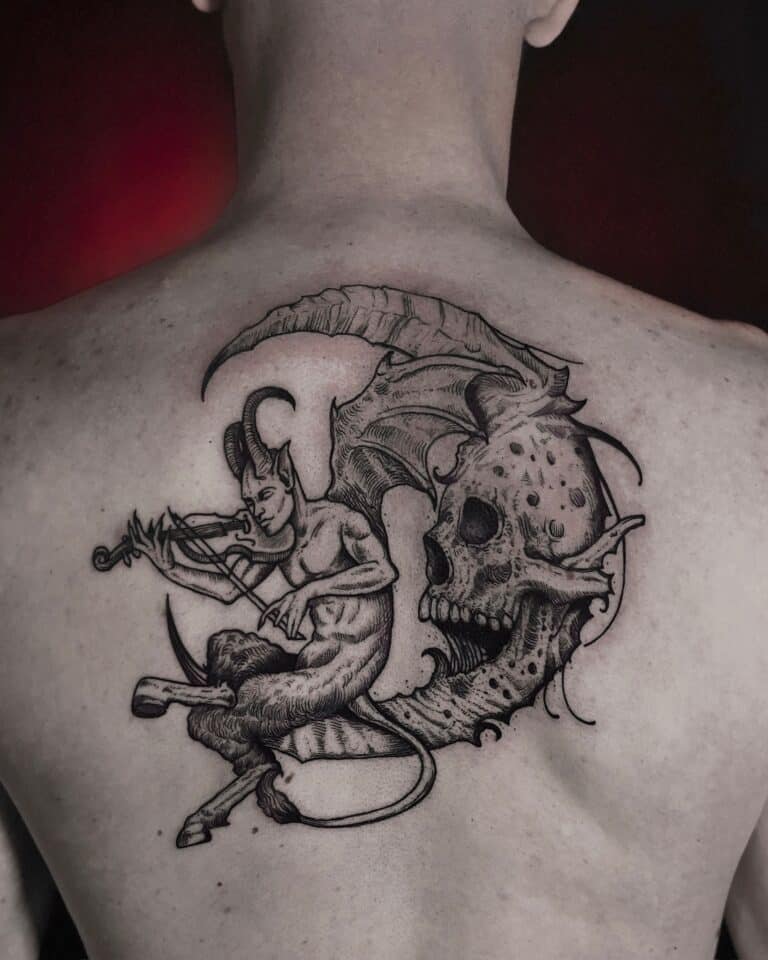 Szczegółowy czarno-szary tatuaż na plecach demona z rogami i ogonem grającego na skrzypcach, siedzącego na gałęzi drzewa obok przesadzonej czaszki z nietoperzowymi skrzydłami i misternymi detalami, osadzony na lekko czerwonej skórze. Wykonany przez renomowane studio Seven Sins Tattoo w Poznaniu, ten obraz uchwycony na zdjęciu „DSC01083” prezentuje prawdziwe artyzm.