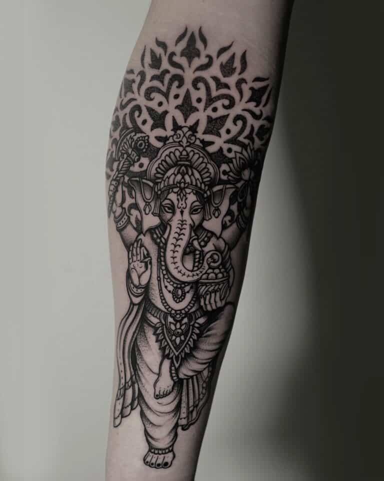7sinstattoo.pl Tatuaż na przedramieniu, przedstawiający czarno-szarą interpretację hinduskiego bóstwa z głową słonia, Ganeshy, prezentuje skomplikowany wzór o nazwie DSC04784. Został stworzony przez artystę z wiodącego studia tatuaży Poznań i zawiera ozdobne detale wokół bóstwa oraz elementy dekoracyjne nad głową Ganeshy. Najlepsze studio tatuażu Seven Sins Tattoo