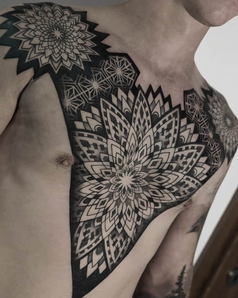 7sinstattoo.pl Osoba z misternymi czarno-szarymi geometrycznymi tatuażami mandali DSC04864 na klatce piersiowej i ramieniu, wykonanymi w najlepszym studio tatuażu w Poznaniu. Tatuaże składają się z warstwowych, symetrycznych wzorów o różnych kształtach i cieniowaniu, pokrywających jedno ramię i rozciągających się na górną część klatki piersiowej. Najlepsze studio tatuażu Seven Sins Tattoo