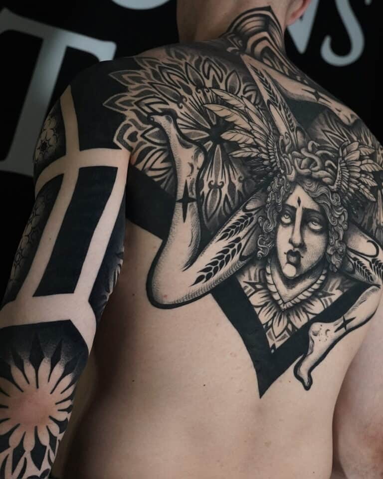 7sinstattoo.pl Osoba z misternym tatuażem pokrywającym ramię i górną część pleców, wykonanym w studio tatuażu Poznań, prezentuje projekt DSC05919. Tatuaż przedstawia szczegółową twarz z misternym nakryciem głowy i ozdobnymi wzorami rozciągającymi się na ramieniu i ramieniu, obejmującymi śmiałe, geometryczne wzory i elementy kwiatowe. Najlepsze studio tatuażu Seven Sins Tattoo
