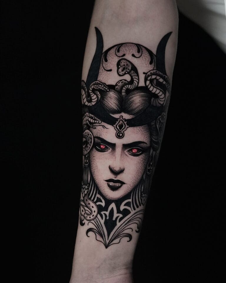 7sinstattoo.pl Tatuaż o nazwie DSC06047 na przedramieniu, przedstawiający szczegółową Meduzę z utworzonymi zamiast włosów, misternym hełmem i świecącymi czerwonymi oczami na czarnym tle. Projekt wyróżnia się precyzyjną linią i cieniowaniem, tworząc mroczną, mityczną atmosferę. Najlepsze studio tatuażu Seven Sins Tattoo