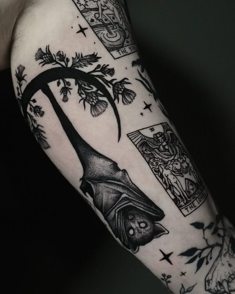 7sinstattoo.pl Tatuaż na ramieniu wykonany w najlepszym studio tatuażu Poznań zawiera misterne wzory wykonane czarnym tuszem, w tym dużego nietoperza wiszącego do góry nogami, elementy kwiatowe i dwie karty tarota oznaczone jako „The Sun” i „The Lovers”. Obszar otaczający obejmuje liście i detale związane z naturą. To oszałamiające dzieło sztuki zostało uchwycone w produkcie DSC07762. Najlepsze studio tatuażu Seven Sins Tattoo