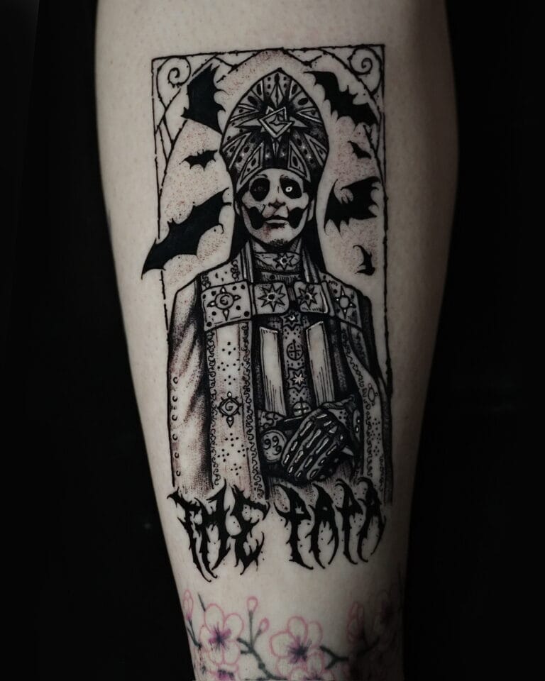 7sinstattoo.pl Tatuaż na ramieniu osoby, uchwycony na zdjęciu DSC09857 ze studia tatuażu Poznań, przedstawia postać w wymyślnych szatach z nakryciem głowy, otoczoną nietoperzami. Wzór umieszczono w prostokątnej ramce. Pod postacią stylizowany tekst brzmi „The Toad”. Kwiaty wiśni zdobią dolną część ramienia. Najlepsze studio tatuażu Seven Sins Tattoo