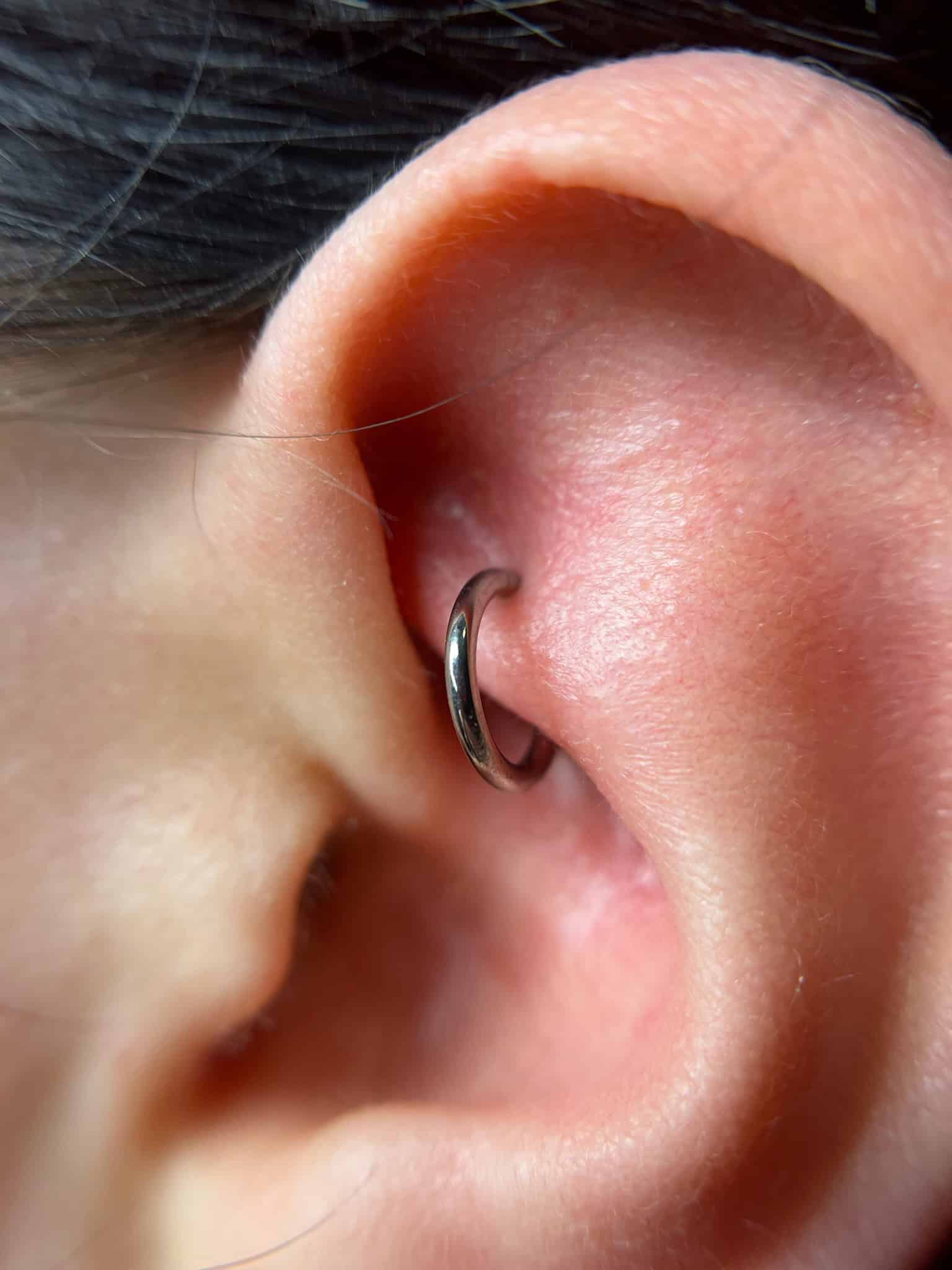 7sinstattoo.pl Zbliżenie ucha osoby z małym, srebrnym kółkiem przebijającym tragus. Skóra wydaje się gładka, a kolczyk jest prosty i nieozdobiony — idealny pokaz minimalistycznej elegancji IMG_8950, często wykonywanej w najlepszym studio tatuażu Poznań. Najlepsze studio tatuażu Seven Sins Tattoo