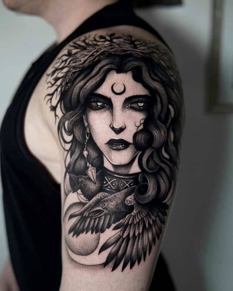 7sinstattoo.pl Osoba ze szczegółowym czarno-szarym tatuażem na górnej części ramienia. Tatuaż „fggdh” Poznań przedstawia kobietę z długimi, falującymi włosami, półksiężycem na czole i dużym ptakiem, prawdopodobnie krukiem, na piersi — z misternym cieniowaniem i elementami wzornictwa. Najlepsze studio tatuażu Seven Sins Tattoo