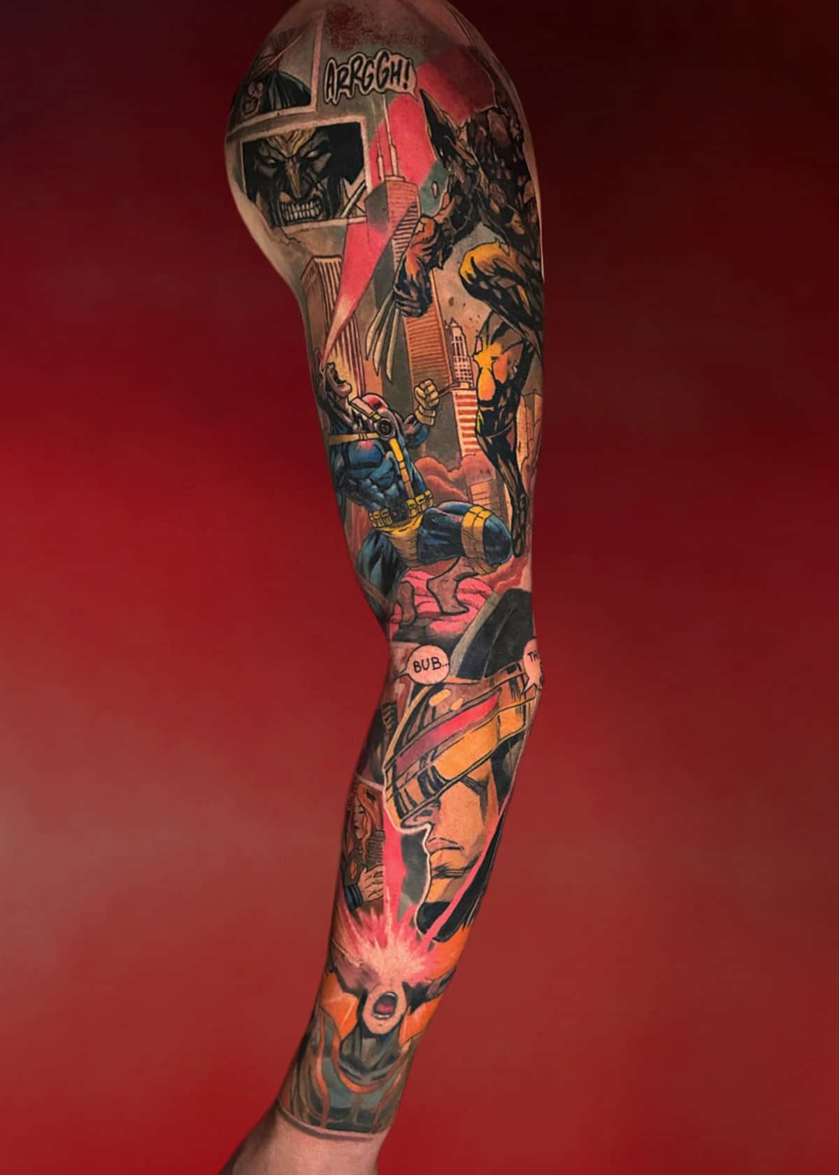 Ramię osoby ozdobione misternym, kolorowym tatuażem na rękawie. Grafika przedstawia postacie z komiksów w dynamicznych scenach akcji, uzupełnionych dymkami i efektami dźwiękowymi, takimi jak „ARGGH!” Tło jest gradientem czerwieni, co wzmacnia żywą i dramatyczną naturę tatuażu.