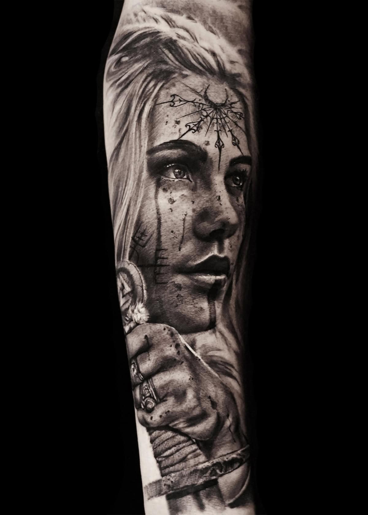 Czarno-biały tatuaż przedstawiający realistyczną twarz kobiety z dokładnym cieniowaniem. Jej twarz zdobią symbole i linie, a ona patrzy w dal. Jej dłonie obejmują rękojeść miecza, ozdobioną skomplikowanymi wzorami. Tło jest ciemne, dzięki czemu szczegółowa grafika się wyróżnia.