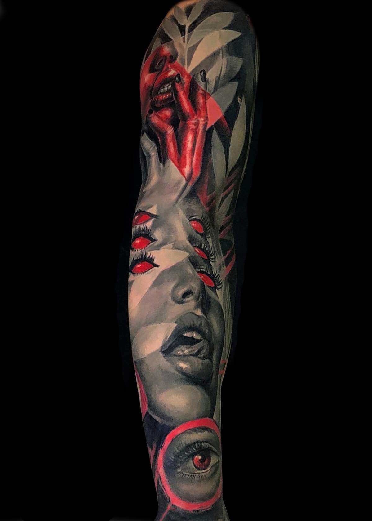 Starannie szczegółowy tatuaż pokrywa przedramię, przedstawiający portrety w skali szarości twarzy wyrażających szereg emocji, przeplatane żywymi czerwonymi akcentami na ustach, oczach i palcach. Dzieło obejmuje geometryczne kształty i oko na dole z jaskrawoczerwoną tęczówką.